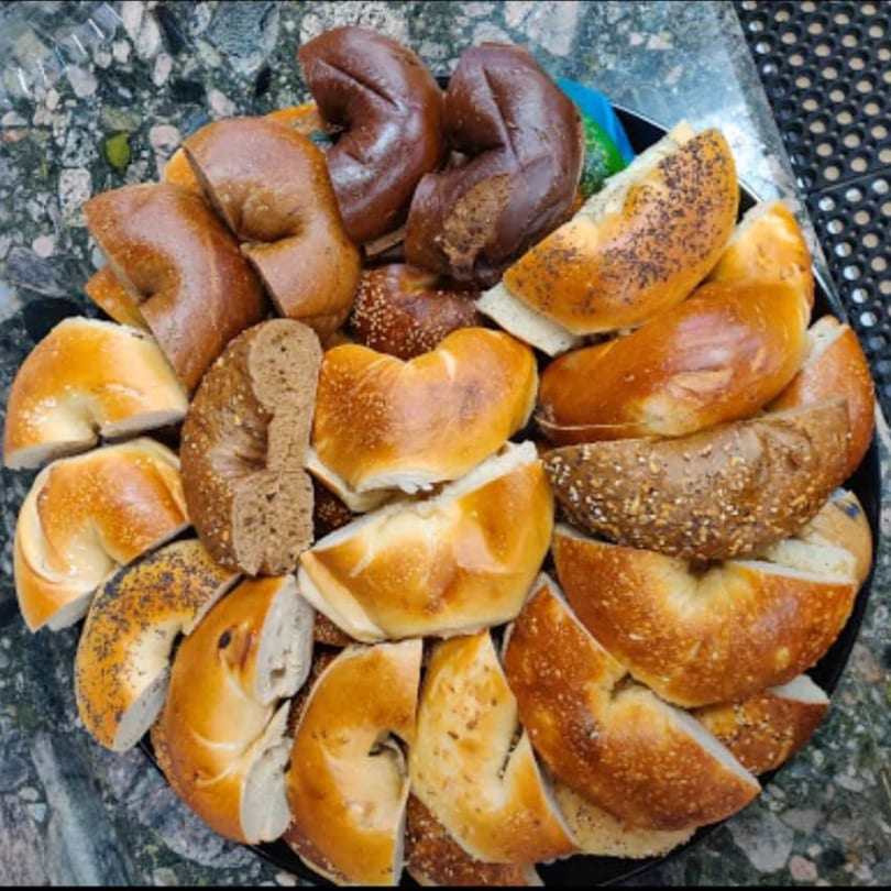 A platter of sliced John's Famous Bagels & Deli bagels, including plain, poppy seed, and dark rye.
