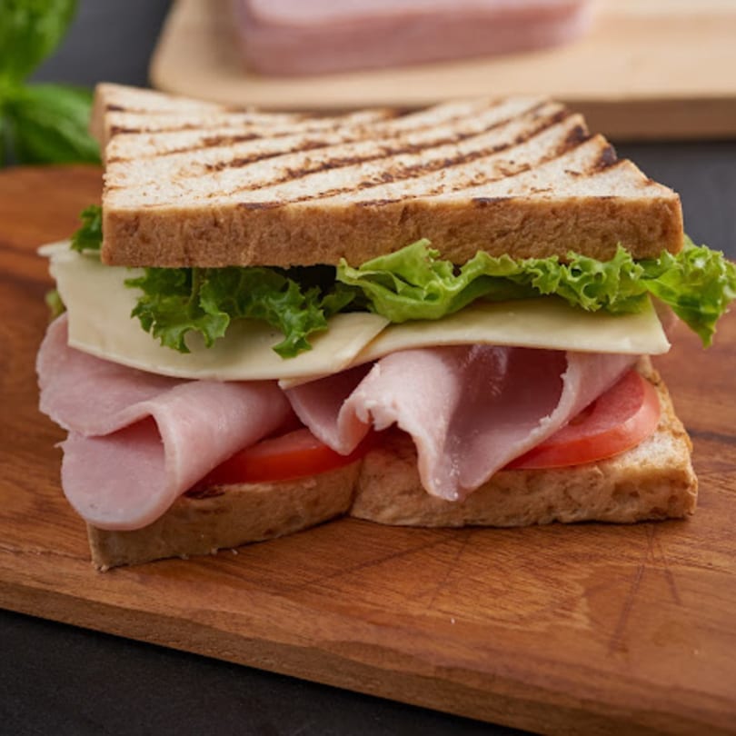 Grilled ham and cheese sandwich with lettuce and tomato on a wooden board.