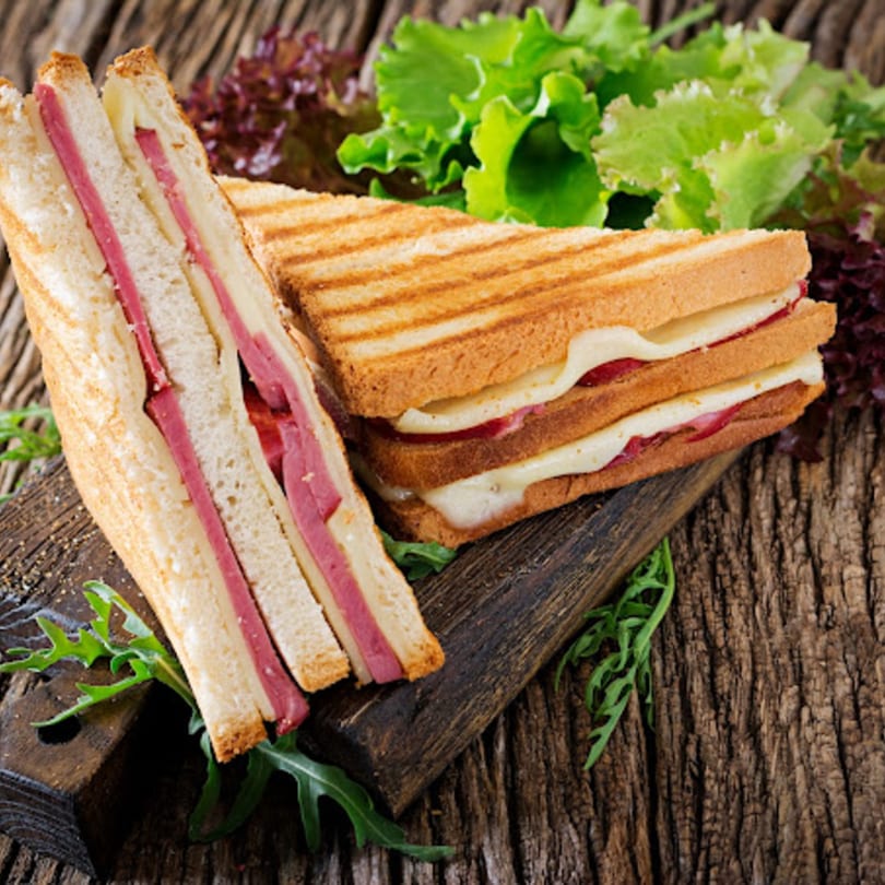 Two grilled deli sandwiches with meat and melted cheese, garnished with fresh lettuce on a wooden board.