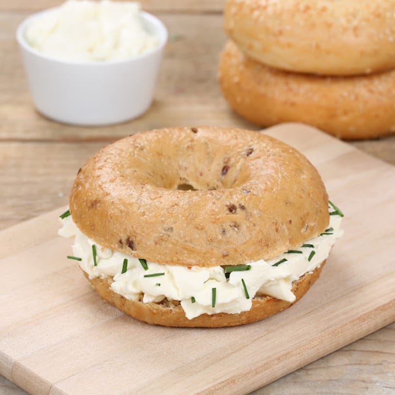 A John's Famous Bagels & Deli bagel with cream cheese and chives on a wooden board.