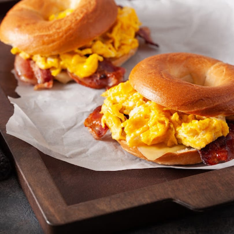 Two John's Famous Bagels & Deli breakfast sandwiches with scrambled eggs, bacon, and cheese.